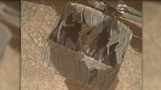 a close-up of a metal wheel with deep cracks and caved-in sections as it rests on a reddish-orange rocky surface