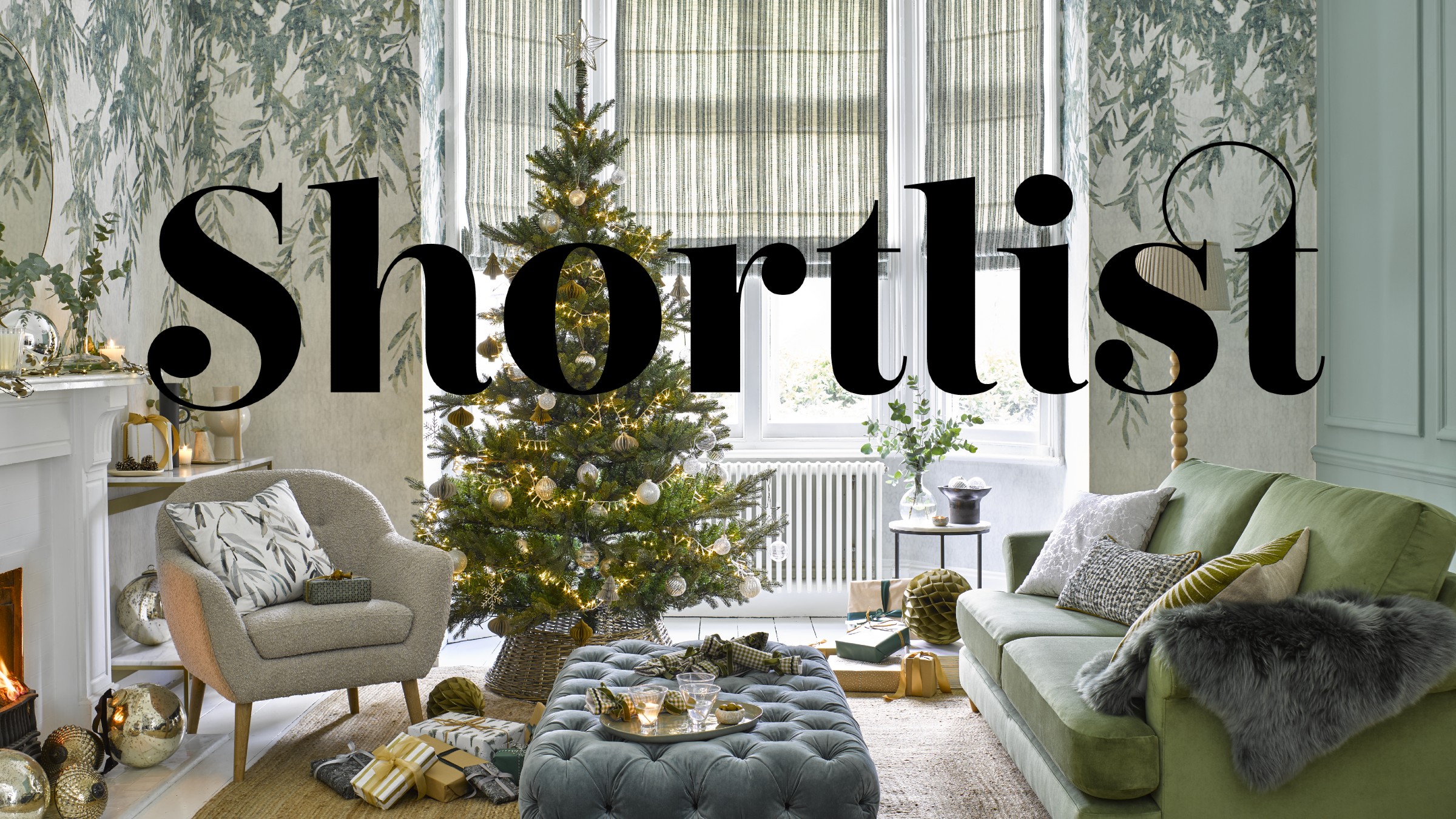 A living room with botanical-print wallpaper and a green sofa decorated for Christmas with a lit-up Christmas tree in the middle of the room