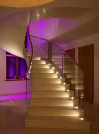 A curved staircase with LED lighting illuminating each step and pink ambient lighting in the background