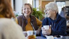 Older women smile and laugh as they talk over coffee in a restaurant.