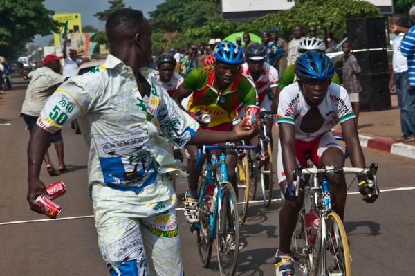 Riders take a Coke handoff in the final circuits of the Benin Independence Race