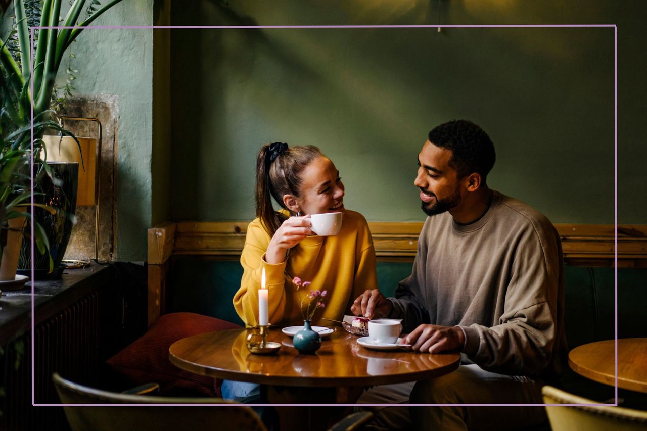 man and woman smiling at each other over cofee with green wall