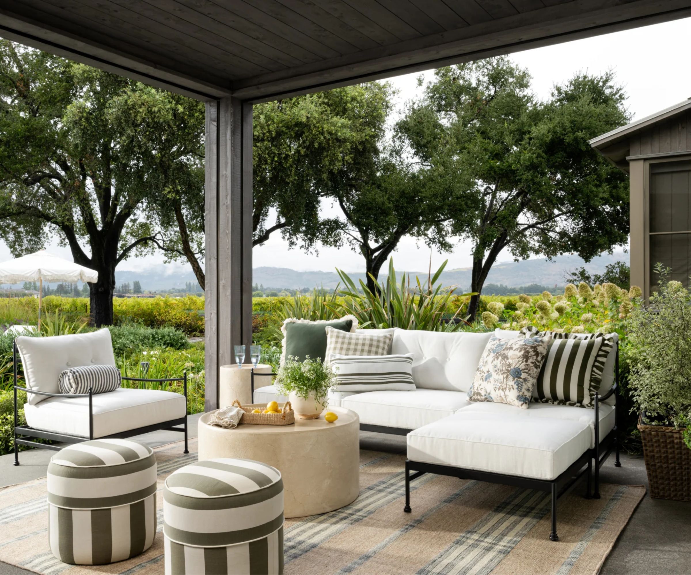 a nappa valley vineyard veranda styled by McGee &amp;amp; Co for their summer outdoor collection with wrought iron furniture, a plaid rug, and striped ottomans