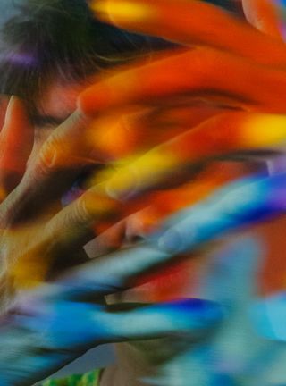 Color effect photo of artist looking through her interlocked fingers