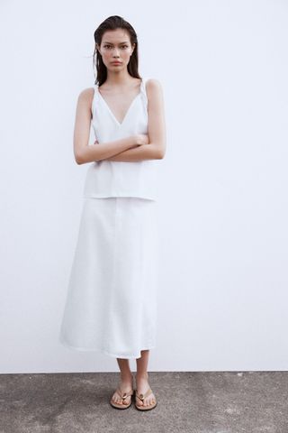 Woman wears white cotton vest top and midi skirt with a pair of suede beige sandals.