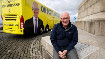John Swinney standing next to promotional material on a bus