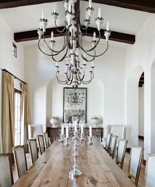 rustic farmhouse table in a large neutral dining room with 2 overhead crystal chandeliers