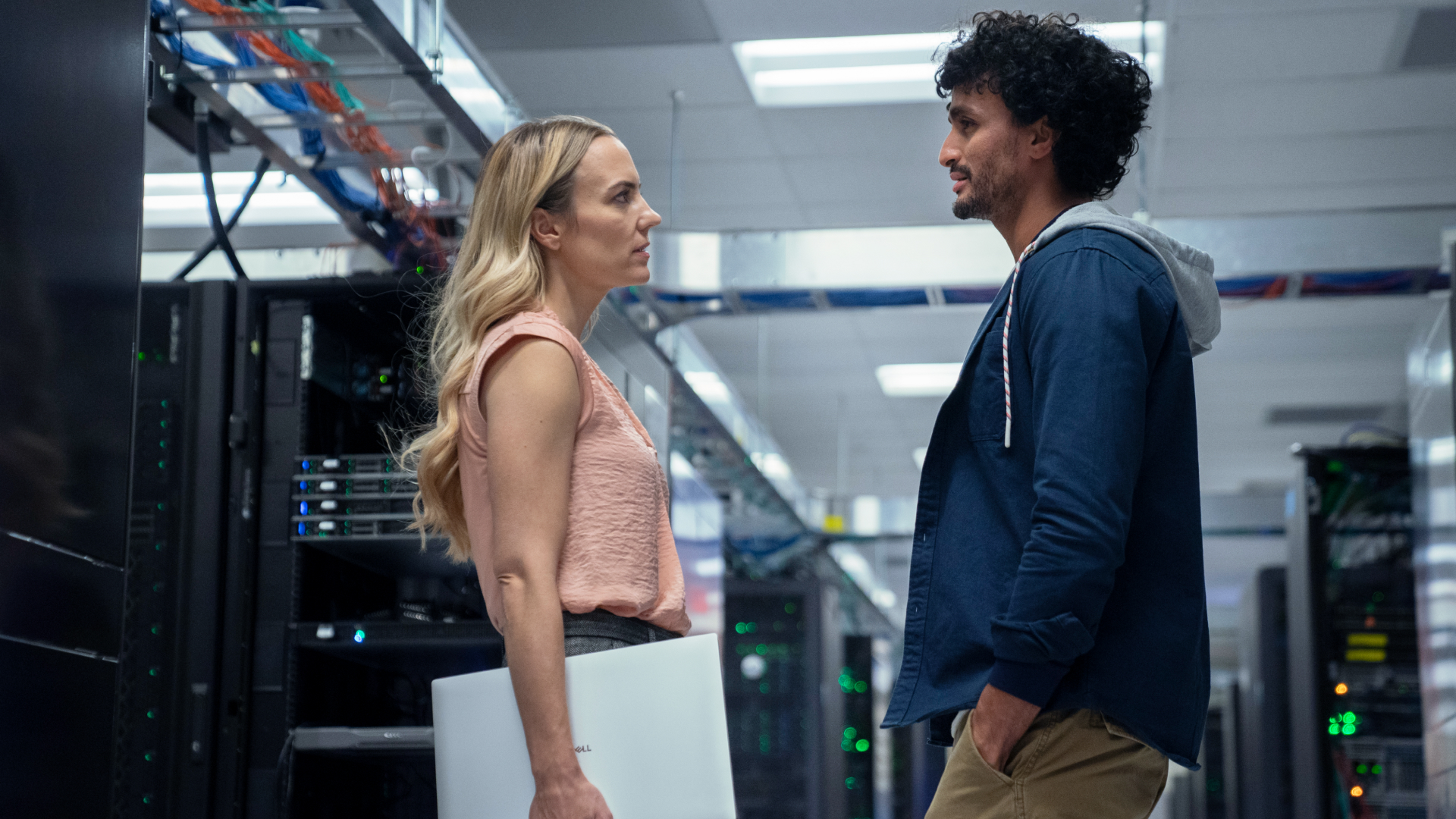 Two people talking to each other in a data center, one is holding a laptop