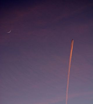 An airplane flies across a purple twilight sky with the crescent moon bright in the background on Dec. 26, 2011 in this photo by skywatcher David Smoyer.