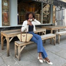 Woman wears a designer Prada basket bag with jeans while sitting on a bench outside a bakery