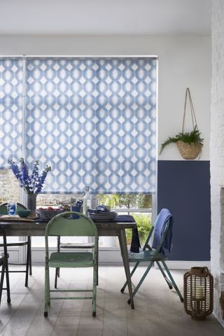 Blue patterned roller blinds in dining room with table and metal sage green chairs
