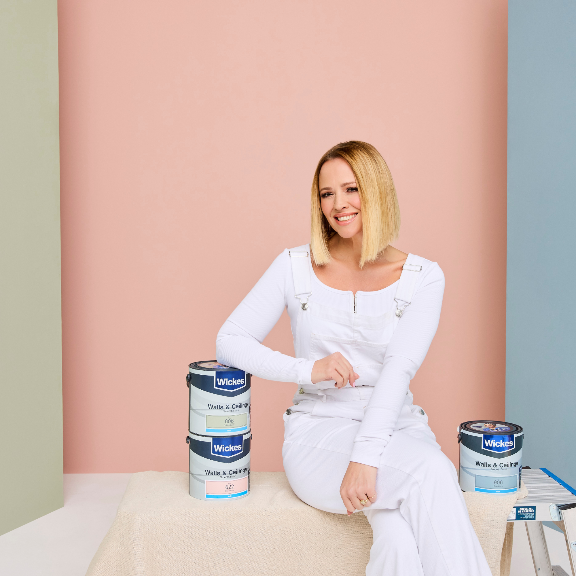 Kimberley Walsh posing with her paint collection, in front of a background painted with blush rose.