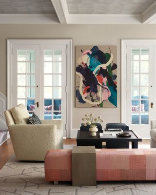 Cream living room with cream boucle armchair, pink ottoman, dark brown gloss coffee table and abstract artwork