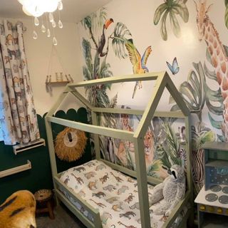 a jungle themed child's room with a green four poster bed, jungle bedding and curtains and a lovely jungle wallpaper feature wall