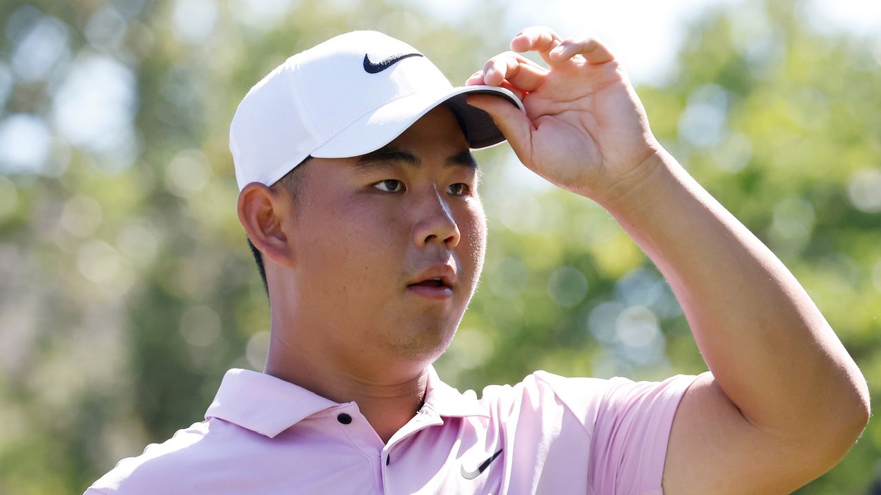 Tom Kim puts his left hand up to his cap brim at the FedEx St Jude Championship 2024