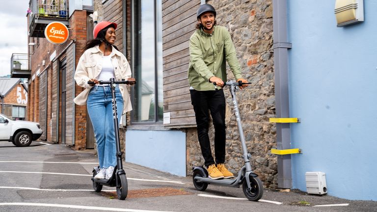 Man and woman riding Pure Air Electric scooters past a shop