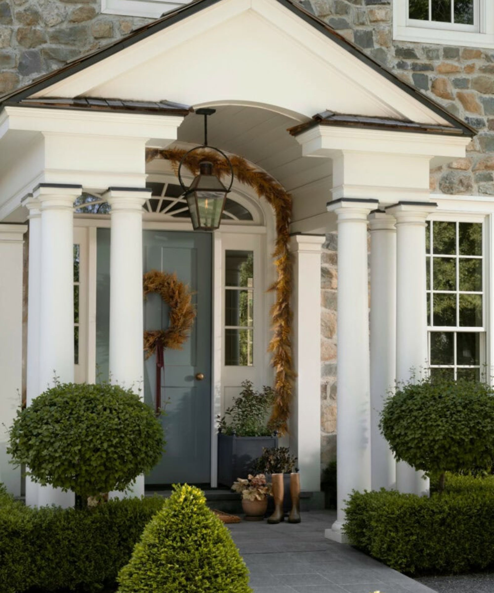 white pillared porch on a stone home decorated for thanksgiving with golden foliage garland and door wreath
