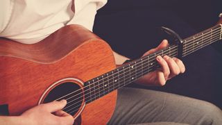 Man plays an acoustic guitar with a capo attached