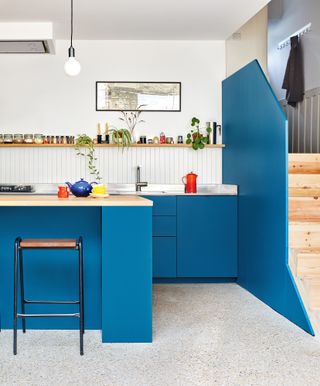 Blue kitchen and island with white vertical splashback tiles and concrete aggregate floor