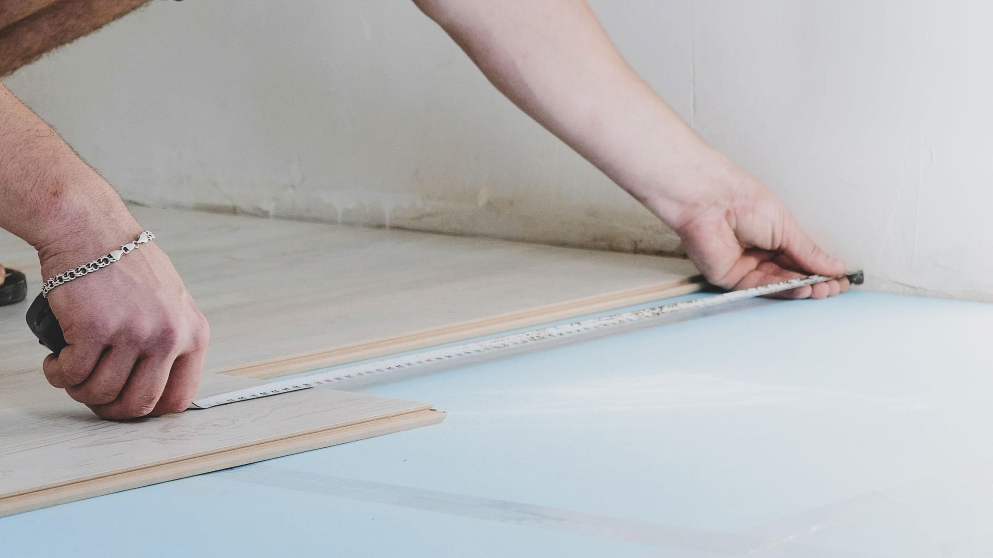 a person measuring between a laminate floor plank and the wall