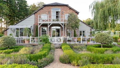 exterior of a converted Victorian house with two side extensions, wooden veranda and balcony and parterre garden