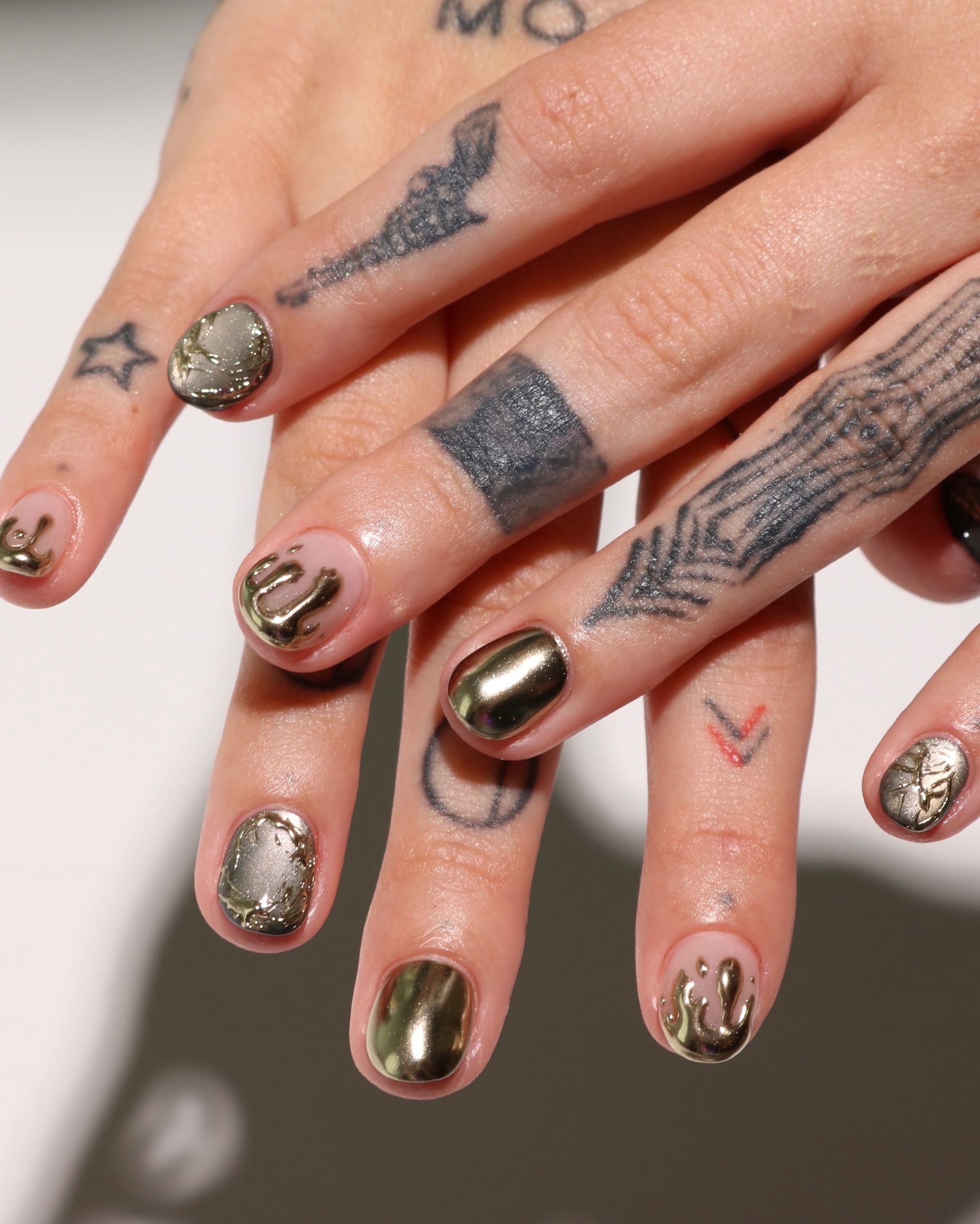 gold chrome and raised metallic drips on short nails, with textured accents and finger tattoos
