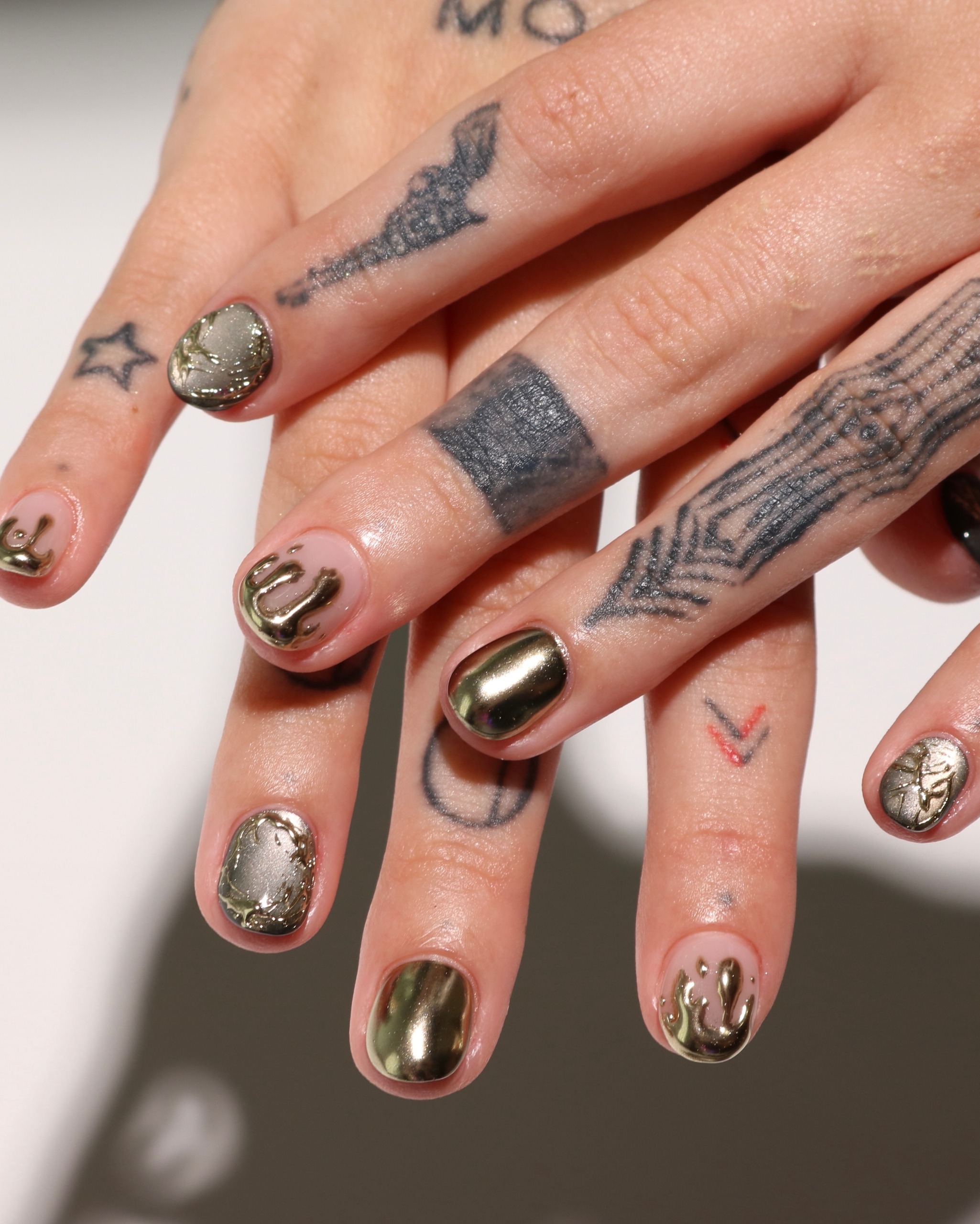 gold chrome and raised metallic drips on short nails, with textured accents and finger tattoos