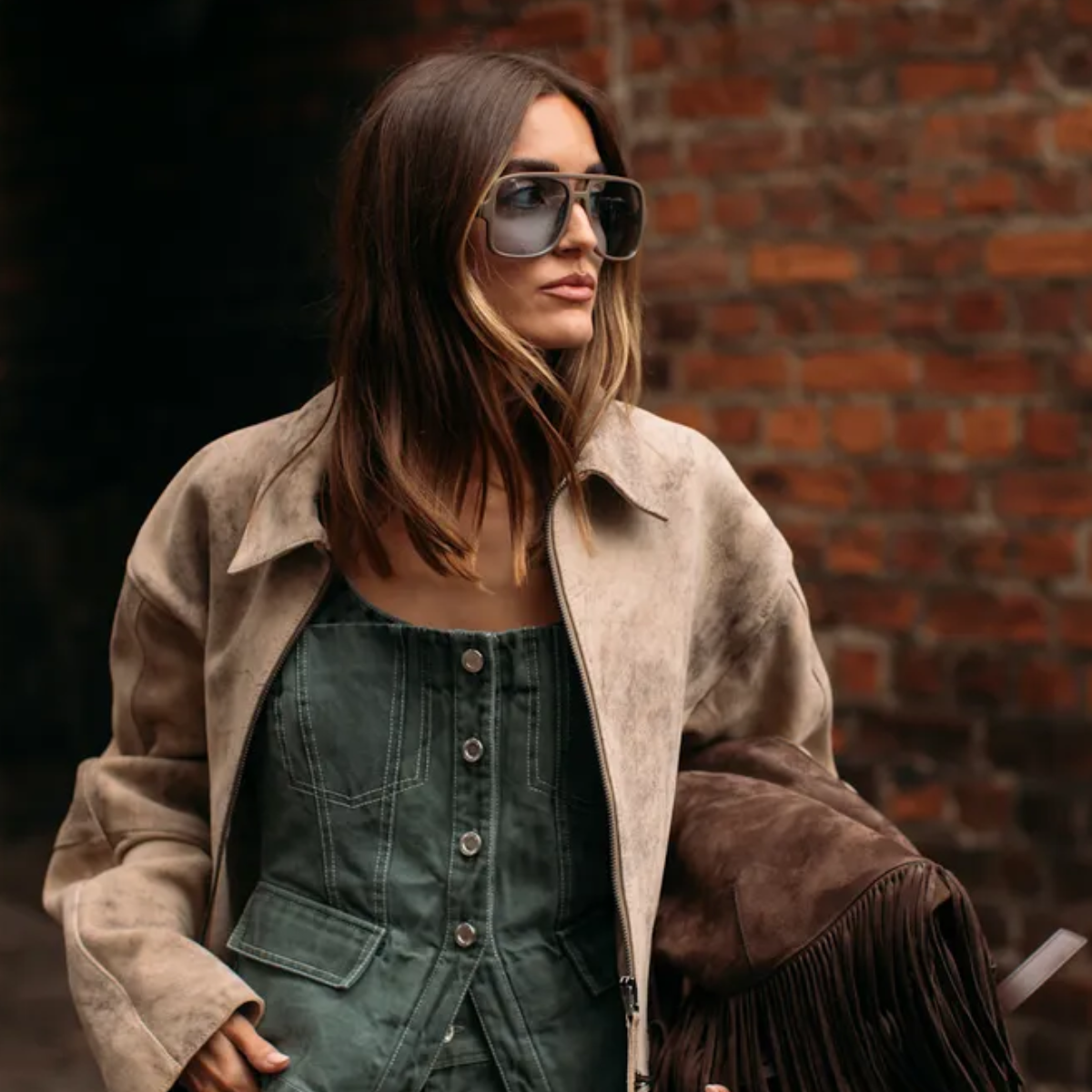 woman wearing a suede jacket and a suede bag and a denim shirt. 