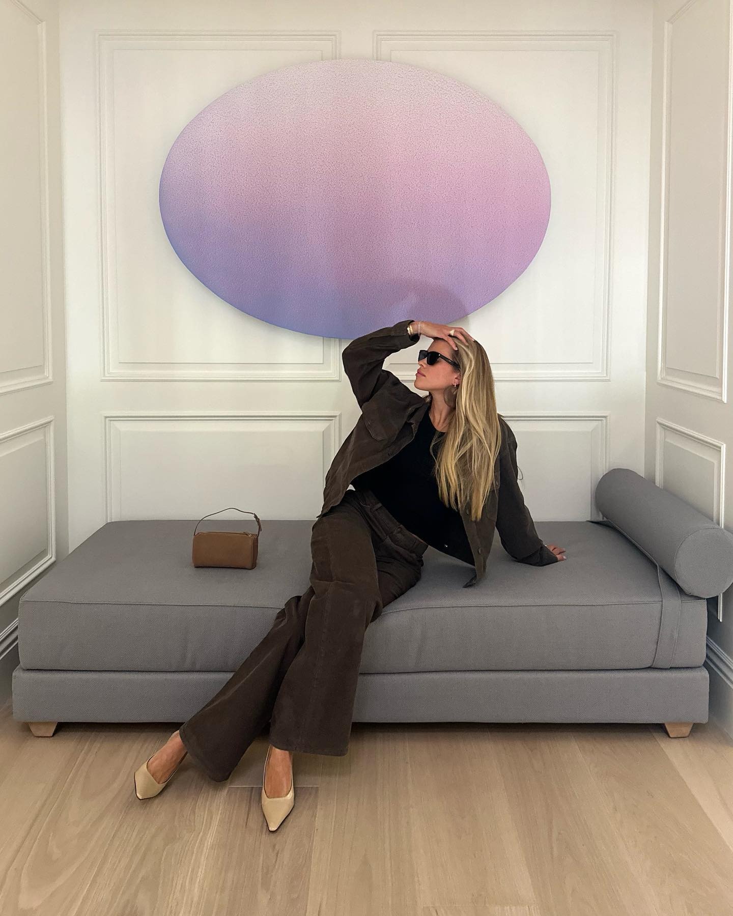 Sofia Richie Grainge sits on a sofa wearing brown jeans with a brown denim jacket and beige pointed-toe heels.