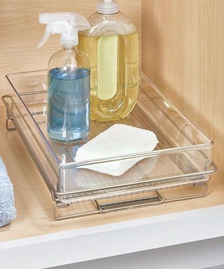 An acrylic and metal sliding under sink storage tray with plastic bottles under sink