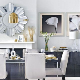 White dining room with white dining chairs, silver edged mirror and golden pendant light