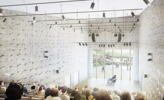 An auditorium in the building with the seating facing towards tall glass windows with a view of an open space. Textured walls and ceiling lights hanging from white ceiling