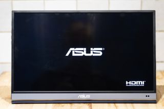 A black and silver ASUS ZenScreen MQ16AH portable monitor on a wooden brown desk