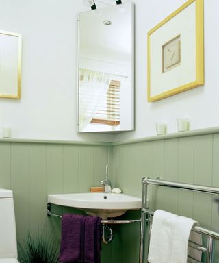 A bathroom with green shiplap paneling, a white corner sink with a purple towel on it, a corner kitchen cabinet and a gold and white wall art print on the wall