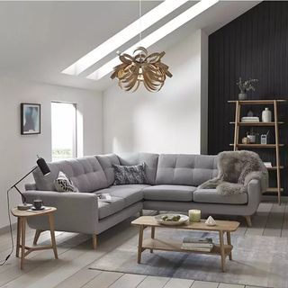 A grey corner sofa with wooden legs in a white living room with a sloping ceiling and wooden side tables
