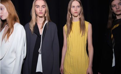 Three models, one wearing a white coat, one in a navy and white coat and one in a yellow dress