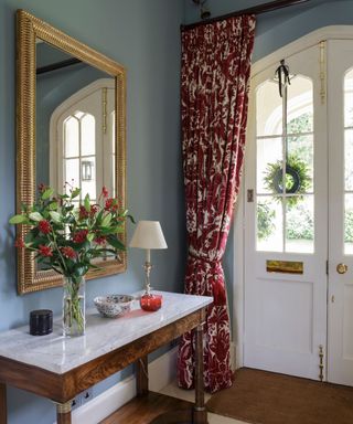 Pale blue hall, marble top console table, Gothic double doors, red draft curtains