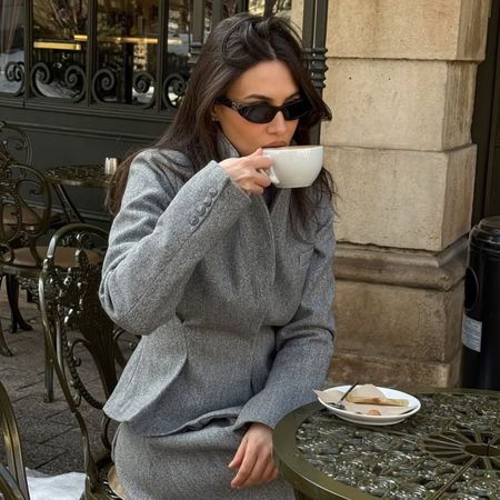An image featuring @borislavasekova drinking a cup of coffee outside in a grey blazer