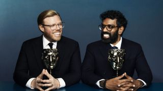 Rob Beckett and Romesh Ranganathan in dark suits sit next to each other with BAFTAs in front of them for the BAFTA TV Awards 2024.