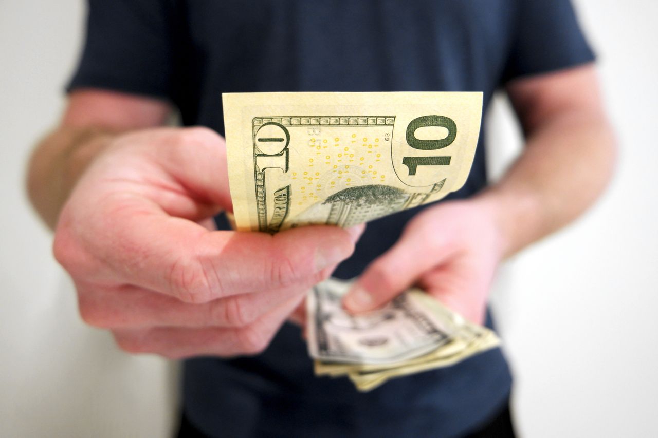 person holding stack of cash in one hand and a ten dollar bill in the other