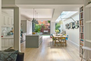 large contemporary kitchen extension at rear of terraced victorian house, with a kitchen island, large dining table, wooden floor and bookcase, photographed by polly eltes