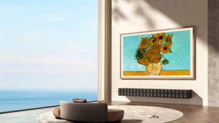 Skyworth Canvas Elite Art TV mounted on a plain wall next to a very large window and a sea view. There is a couch in the photo that looks very small compared to the 100-inch TV