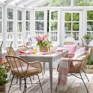 A large white conservatory with a dining table and rattan chairs