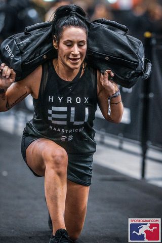 Writer Sam competing at Hyrox performing a lunge holding a sandbag on her back