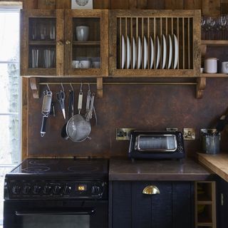Dark blue kitchen cabinets in brown walled kitchen with kitchen items stored on wall