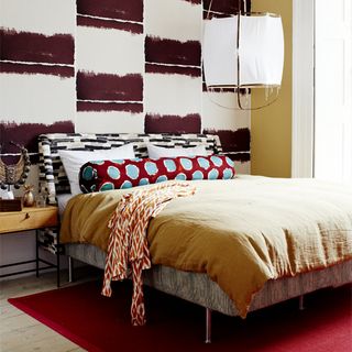 Colourful bedroom with black and white feature wall, yellow and red bed linen and side table