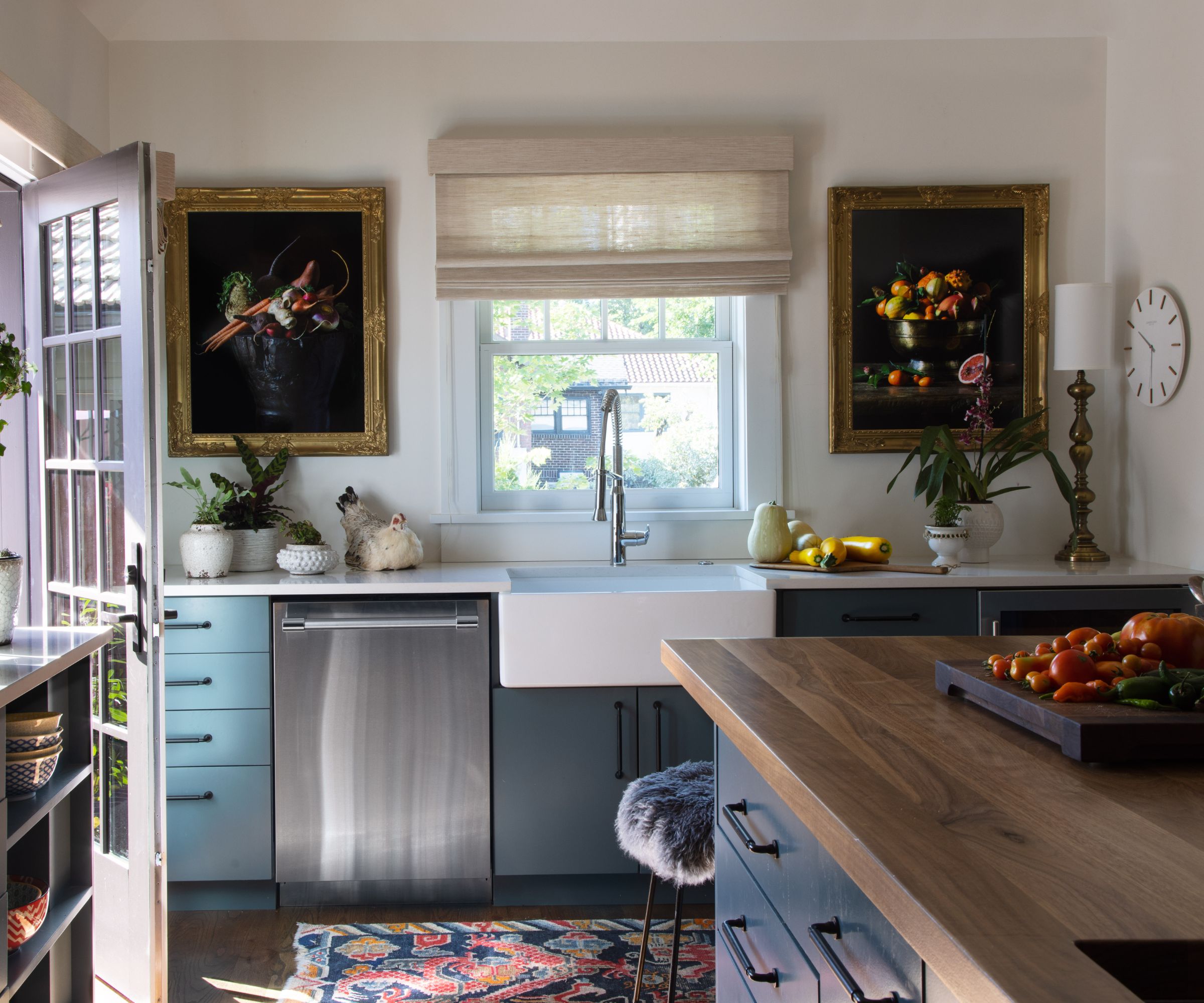 A blue and white kitchen decorated for winter with vases of greenery, layered window treatments, and a colorful runner rug along the main work area