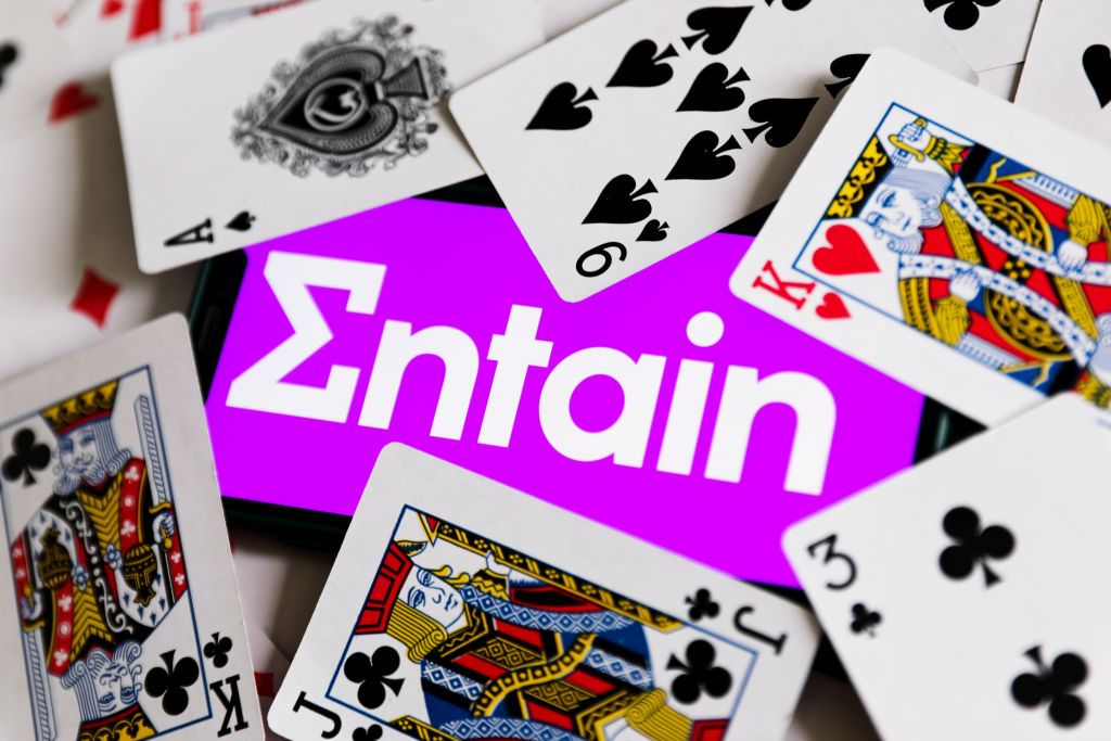 Entain logo displayed on a phone screen is seen with playing cards