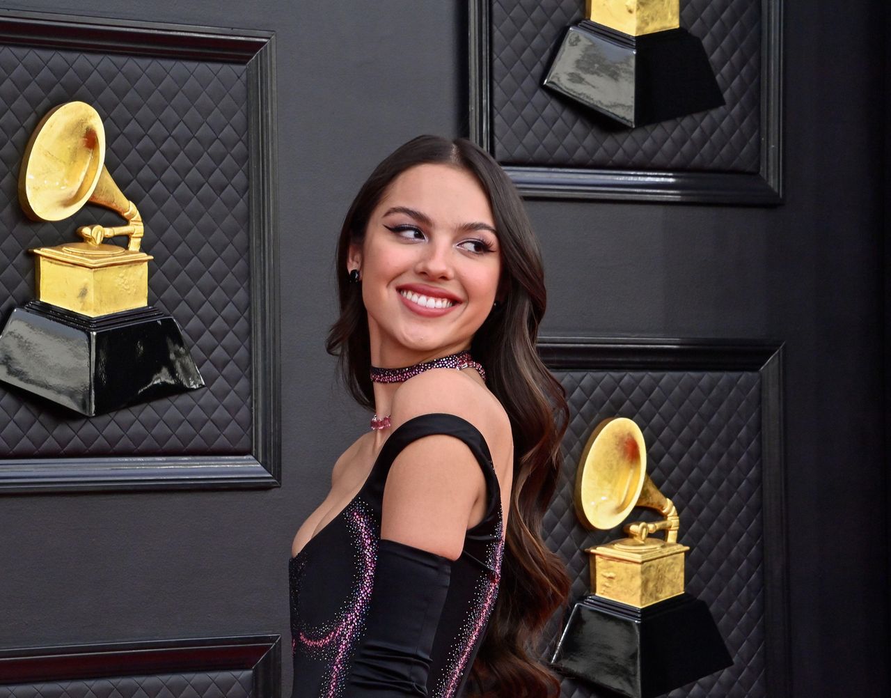 Olivia Rodrigo in a black dress at an awards show.