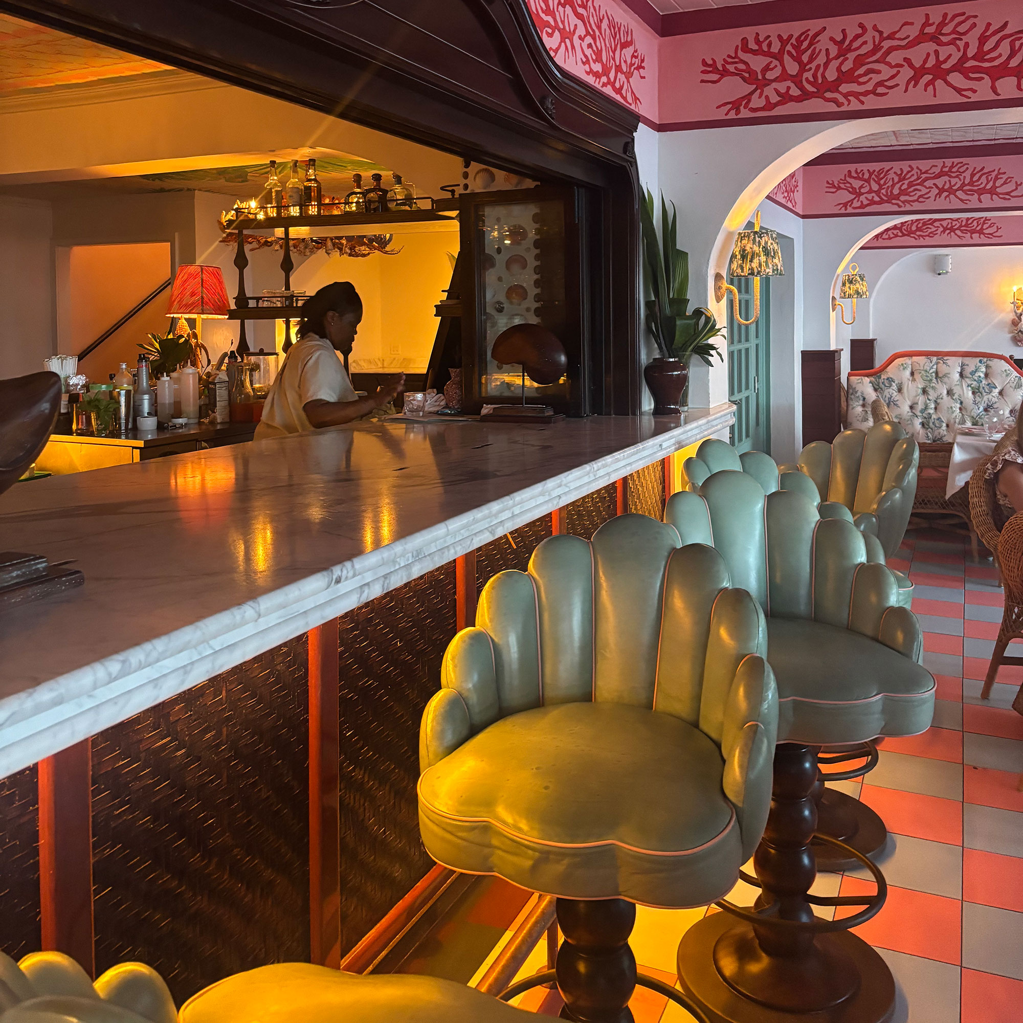 Marble topped bar surrounded by scalloped mint green bar stools on pink and green chequered floor